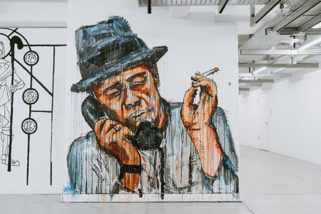 Zdjęcie przedstawia współczesny obraz ciemnoskórego mężczyzny w kapeluszu, który pali papierosa i trzyma słuchawkę stacjonarnego telefonu przy uchu. To ilustracja artykułu o tym, czym jest selfpzblishing.