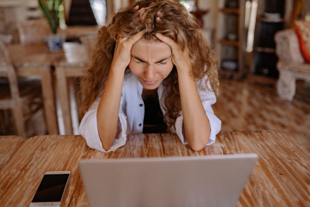 Kobieta siedzi przed laptopem, łapie się za głowę. Na jej twarzy widać frustrację.